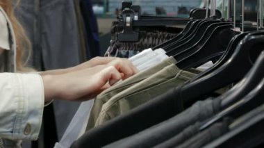 Kadın dükkanda raflar üzerinde asılı olan gömlek bakar. eller bir raf Giysi, bir butik tarama rastlamak. Raf odaklanılan kafa görünümü.