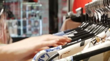 Kadın dükkanda raflar üzerinde asılı olan gömlek bakar. eller bir raf Giysi, bir butik tarama rastlamak. Raf odaklanılan kafa görünümü.