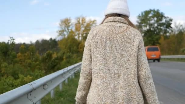 Utazó nő stoppolt egy napos úton és sétált. Fiatal boldog hátizsákos nő keres egy fuvart, hogy elindítson egy utazást egy napfényes vidéki úton. — Stock videók