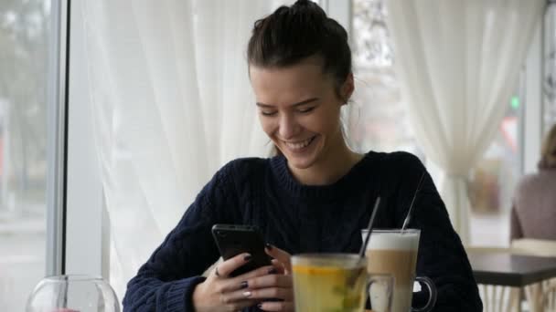 Mujer bonita joven usando teléfono inteligente en la cafetería, beber café en taza, desayuno dulce, cara feliz, retrato hipster al aire libre, chica de la moda, mesa, café con leche sabroso dulce, teléfono de llamada — Vídeos de Stock