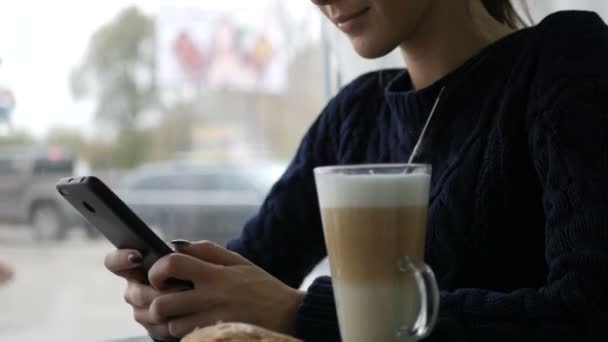 Mulher bonita nova usando smartphone no café, beber café na xícara, café da manhã doce, rosto feliz, retrato hipster ao ar livre, menina da moda, mesa, café com leite saboroso doce, telefone de chamada — Vídeo de Stock