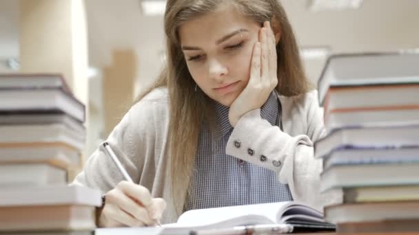 Estudante estudando e tomando notas na biblioteca cercada por livros na faculdade — Vídeo de Stock