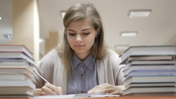 Estudiante que estudia y toma notas en la biblioteca rodeada de libros en la universidad — Vídeos de Stock