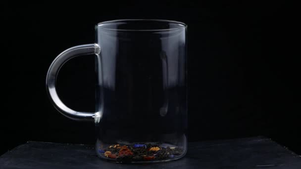 Macro chupito de verter agua hervida en hojas de té en taza de vidrio. Preparación de té negro. Macro disparo del proceso de elaboración de té de hierbas en una tetera transparente de vidrio — Vídeos de Stock
