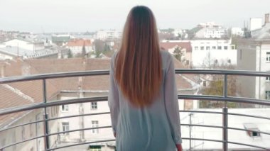 Genç bir kadın için korkuluk balkon gider ve kentin peyzaj hayran