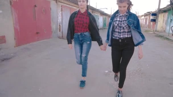 Dos chicas caminando cogidas de la mano en los garajes del gueto. posiblemente lesbianas, hermanas o novias. sacudir efecto cámara — Vídeo de stock