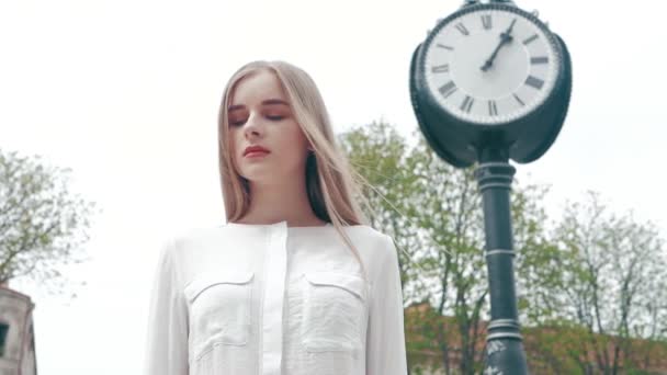 Nyári életmód divat portré fiatal gyönyörű szőke elegáns csípő nő mellett az utcai óra fehér inget visel. kap az elvesztegetett időt. múlandóság az élet — Stock videók