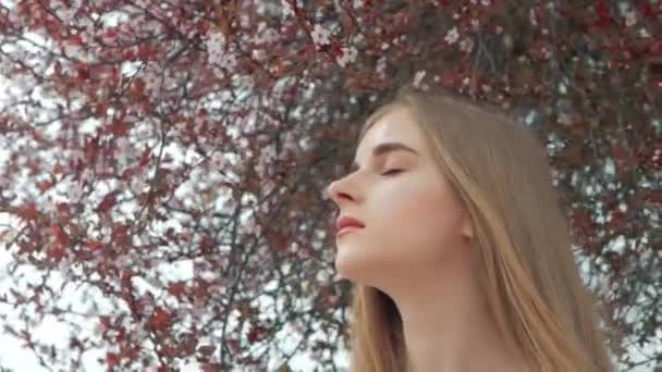 Estilo de vida de verano retrato de moda de joven hermosa rubia mujer hipster elegante con camisa blanca contra el fondo de un árbol floreciente — Vídeos de Stock