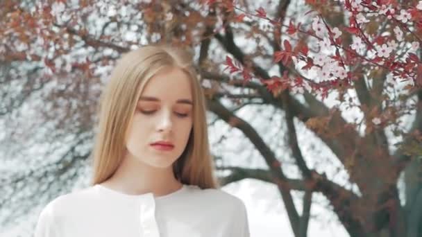Yaz yaşam tarzı moda bir çiçekli ağaç arka planı beyaz gömlek giymiş genç güzel sarışın şık hipster kadın portresi — Stok video