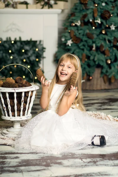 Веселая маленькая девочка играет с конусами на фоне елки — стоковое фото