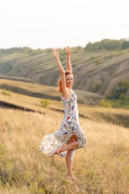 Güzel kızıl saçlı kız gün batımında bir tarlada dans edip eğleniyor..