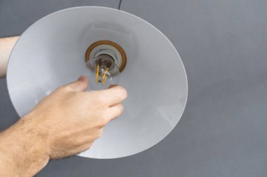 Yakın plan. Bir el şık bir çatı katı lambasında ampulü değiştirir. Spiral filament lamba. Modern iç dekorasyon