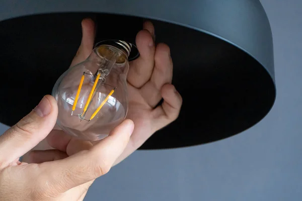 Close-up. A hand changes a light bulb in a stylish loft lamp. Spiral filament lamp. Modern interior decor