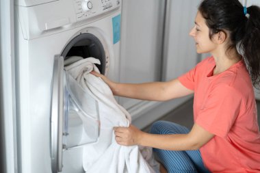 Kirli çamaşırları bir dairede yerde otururken çamaşır makinesine atan bir kız. Çamaşır günü, ev işi..