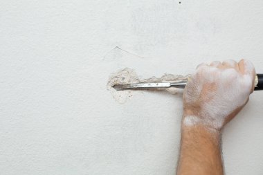 Binanın tamiri. Bir adam duvara kablo döşemek için hendek kazar. Duvara elektrik kabloları döşeniyor.