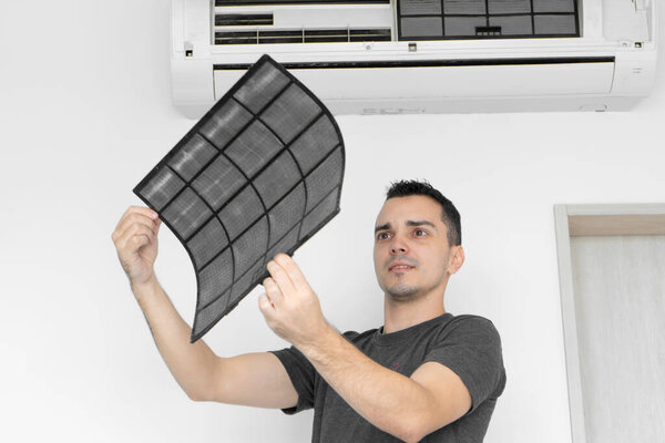 The guy cleans the filter of the home air conditioner from dust. The guy snayed a very dirty air conditioning filter. and examines it in his hands. Climate equipment care