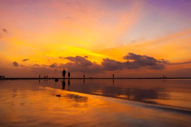 Tropikal bir plajda gün batımında yanan parlak gökyüzü. Göç sırasında gün batımı, suyun üzerinde yürüyen insanların gücü..