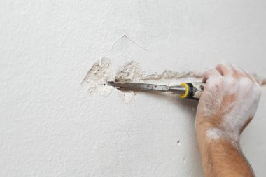 Binanın tamiri. Bir adam duvara kablo döşemek için hendek kazar. Duvara elektrik kabloları döşeniyor.