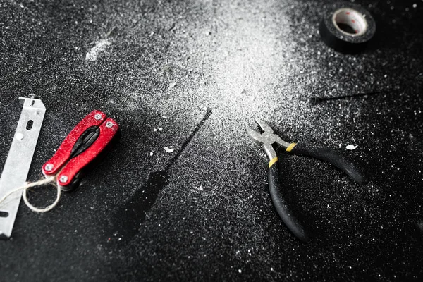 A set of tools for self-installation of the lamp lies on a black table, sprinkled with white dust. Husband for an hour. Household chores