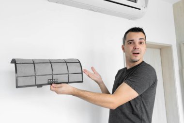 Adam evdeki klimanın filtresini tozdan temizliyor. Çok kirli bir klima filtresi. İklim ekipmanı bakımı