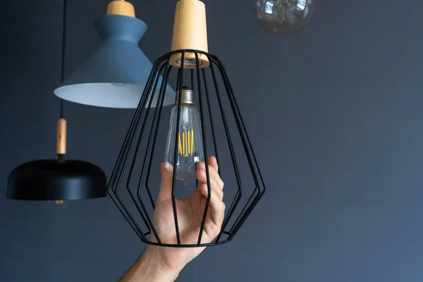 Close-up. A hand changes a light bulb in a stylish loft lamp. Spiral filament lamp. Modern interior decor