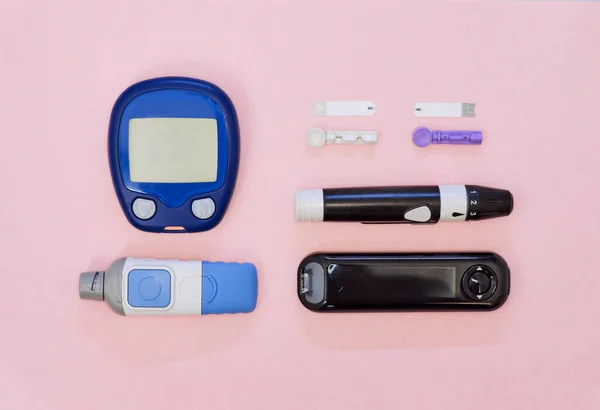 Diabetic kit: two types of glucometers, test strips, lancet. Top view, pink background.