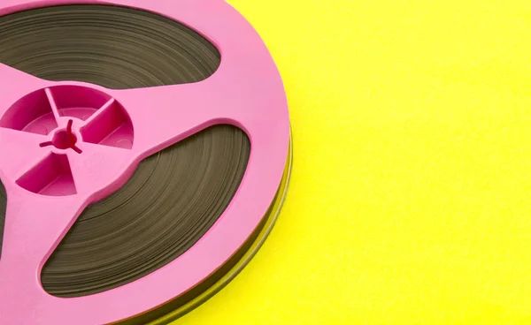 Vintage pink audio reel with recording tape on yellow paper background. Trendy pop art style.