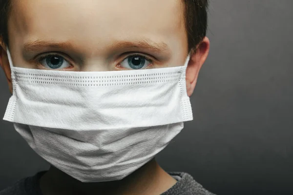 Face of a mask-wearing boy with fear in the eye Close-up on a gray background