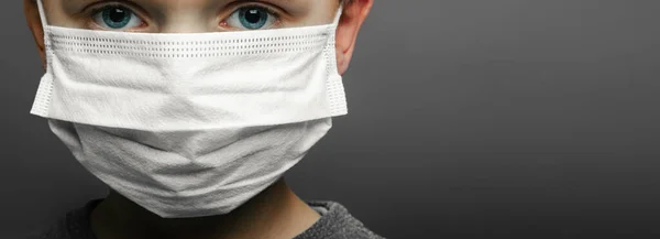 Face of a mask-wearing boy with fear in the eye Close-up on a gray background