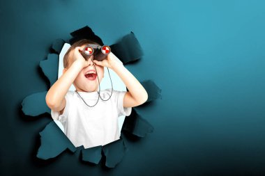 Mutlu çocuk siyah kağıttaki yırtık bir delikten dürbünle bakıyor.