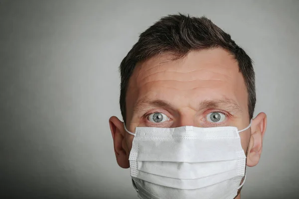 Face of a mask-wearing man with fear in the eye Close-up on a gray background