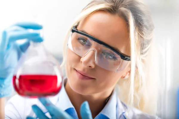 Jonge aantrekkelijke vrouwelijke wetenschapper houden een kolf met blauwe liqu — Stockfoto