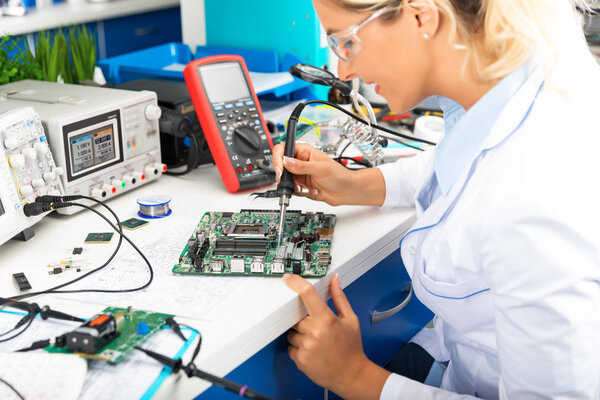 Young female electronic engineer soldering computer motherboard 