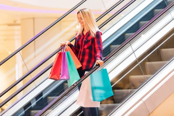 Mujer joven con bolsas de compras en escaleras mecánicas en la tienda de moda —  Fotos de Stock