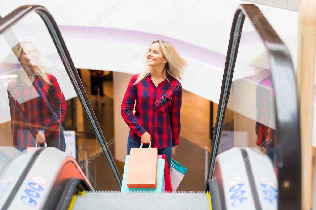 Young woman with shopping bags on escalator in the fashion store