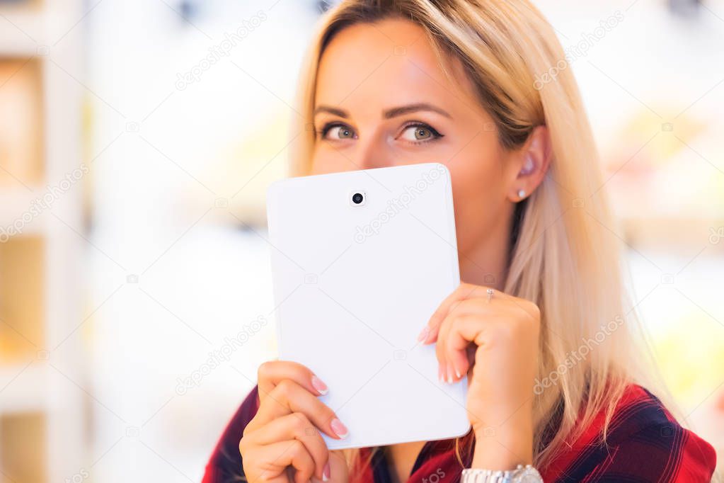 Young attractive woman hides her smile with a tablet computer