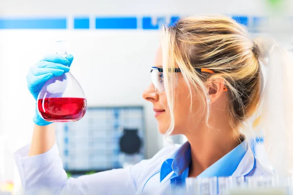 Joven científica atractiva sosteniendo un frasco con licor rojo —  Fotos de Stock