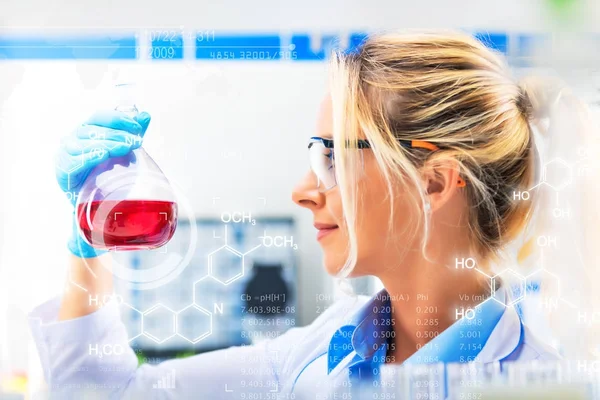 Jovem cientista feminina atraente segurando um frasco com licor vermelho — Fotografia de Stock