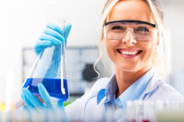 Bir şişesi ile mavi sıvıyla tutan genç çekici kadın bilim adamı