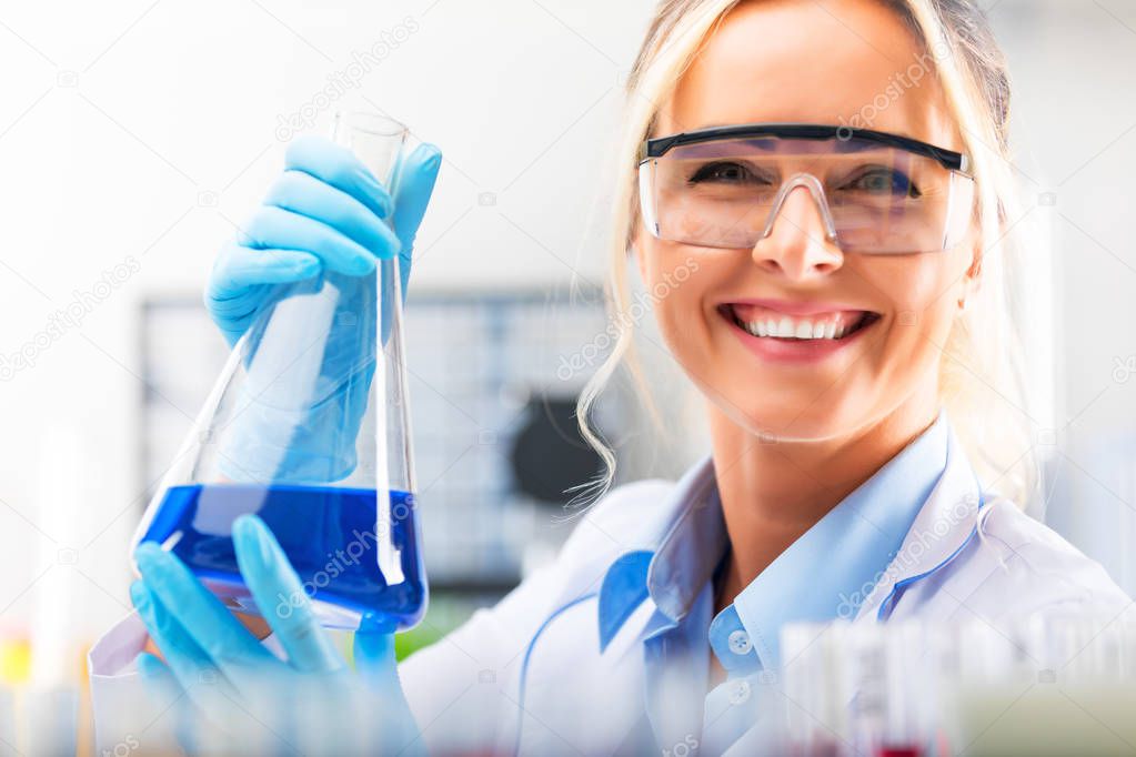 Young attractive female scientist holding a flask with blue liqu