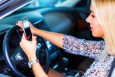 Bir araba sürüş sırasında bir akıllı telefon kullanan genç kadın