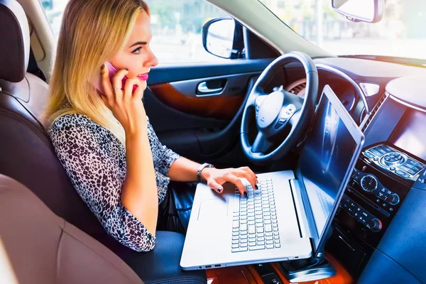 Mulher usando um laptop e smartphone em seu carro — Fotografia de Stock