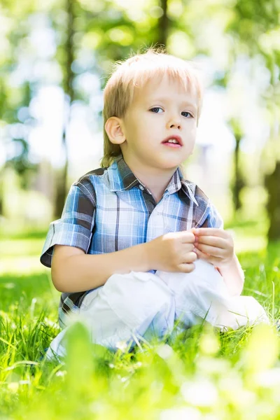 Kleiner Junge sitzt auf dem Gras im Park — Stockfoto