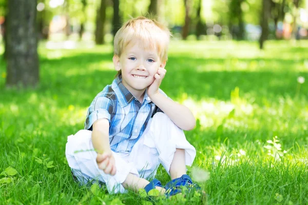 Liten pojke sitter på gräset i parken — Stockfoto