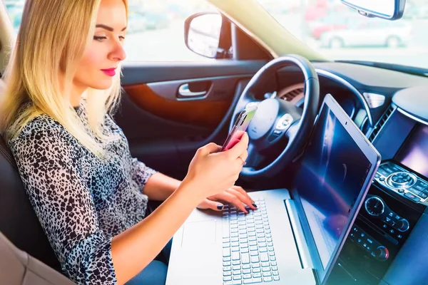 Mulher usando um laptop e smartphone em seu carro — Fotografia de Stock