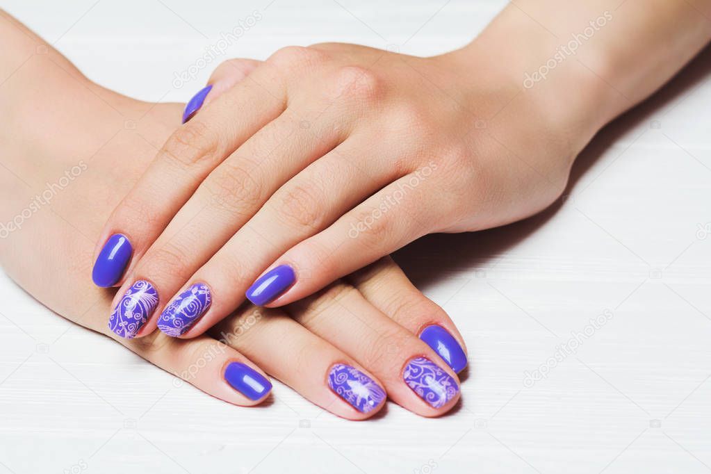 Purple nail art with pink floral pattern on white wooden background