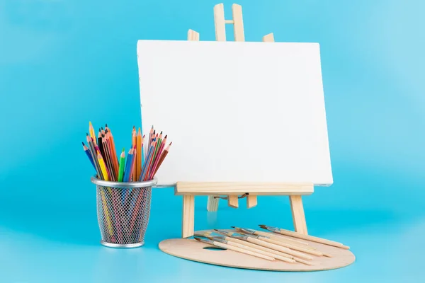 青い背景の上に空白のキャンバス ブラシ カラフルな鉛筆で木製のイーゼル — ストック写真