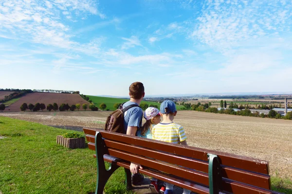 Happy family sitting on bench at meadow at summer day — Stock Photo, Image