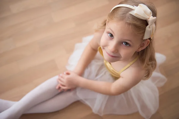 Portret uśmiechający się bardzo staranna balet dziewczynka siedzi w biały — Zdjęcie stockowe