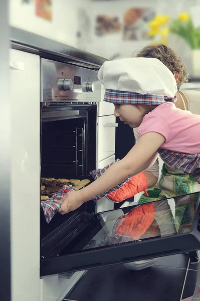 Милая маленькая девочка со своей матерью печет печенье в духовке — стоковое фото